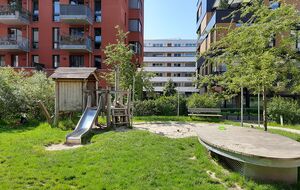 Naturnaher Spielplatz mit Grünflächen und Sitzmöglichkeiten in moderner Wohnanlage